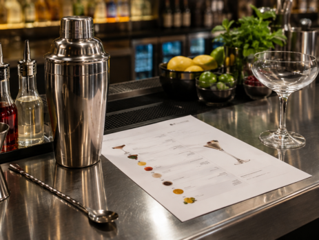fișă băutură bar pe blat de lucru, lângă shaker, dozator și pahar de servire într-un bar profesional