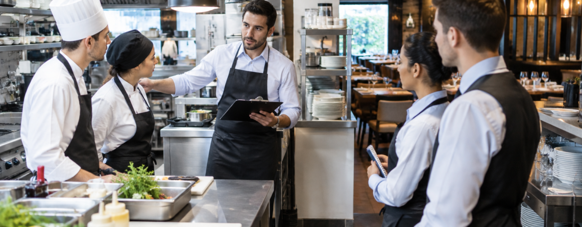integrare angajați HoReCa într-un restaurant profesionist, cu manager care instruiește personal nou în bucătărie și sală